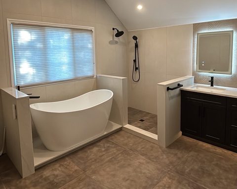 Bathroom before glass: a freestanding tub and a bare tiled shower between knee walls